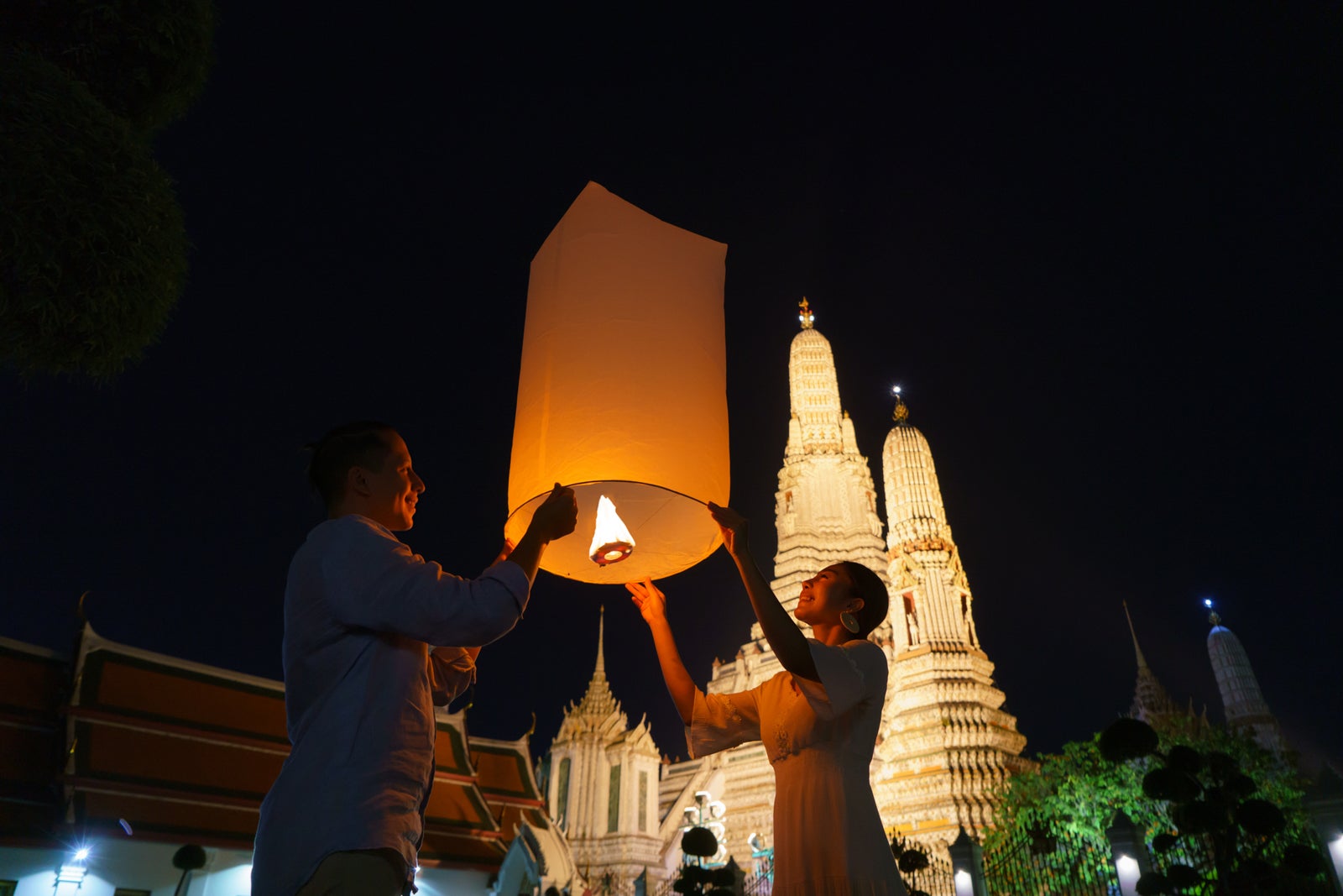 Mixed race romantic lover couple in Wat arun in night time and floating lamp in Yi Peng festival under Loy Krathong day, Bangkok city ,Thailand