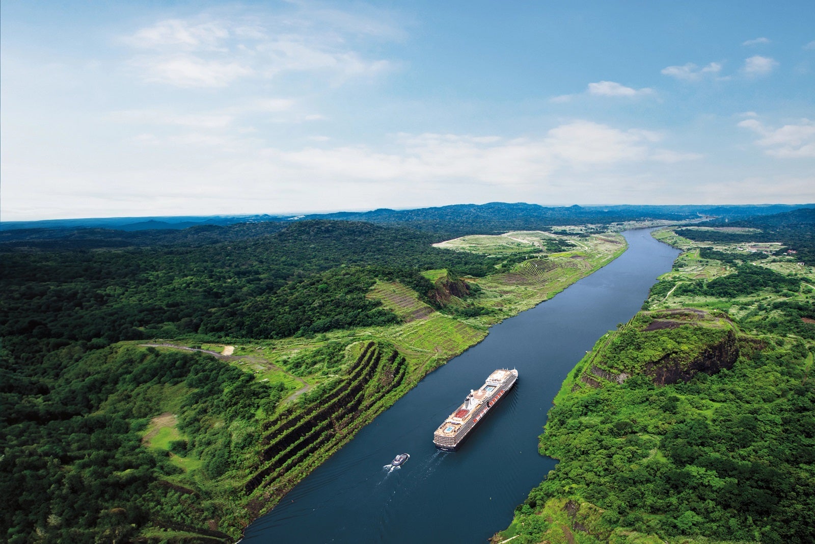 An aerial view of a cruise ship sailing through the Panama Canal with green vegetation on both sides
