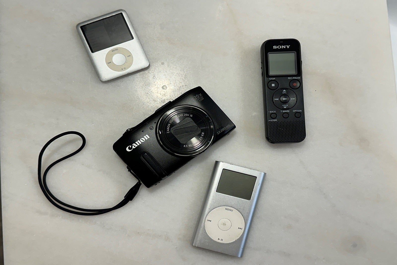 A digital camera, two iPods and a voice recorder sitting on a countertop