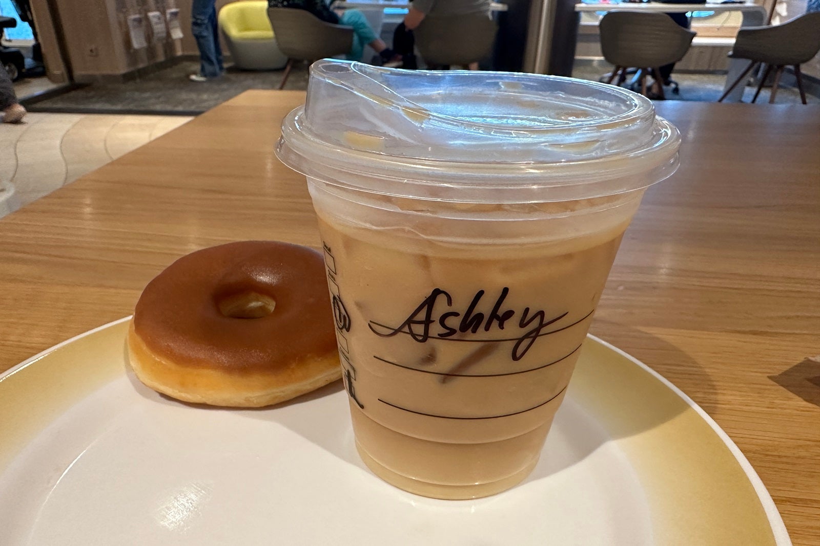 A caramel dougnut next to a cup of iced coffee on a white countertop