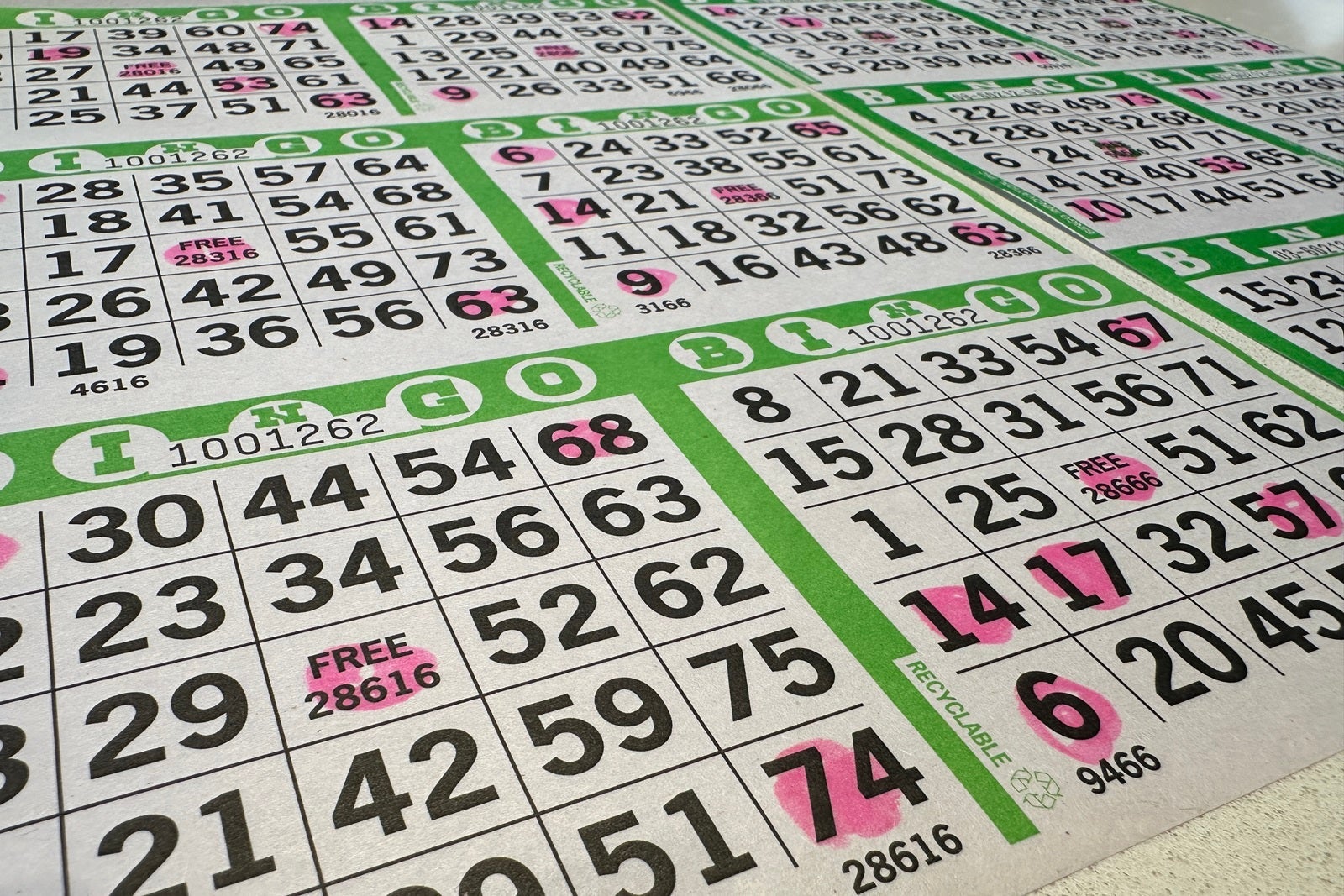 A close-up photo of BINGO cards outlined in green with pink spots marking off numbers that were called