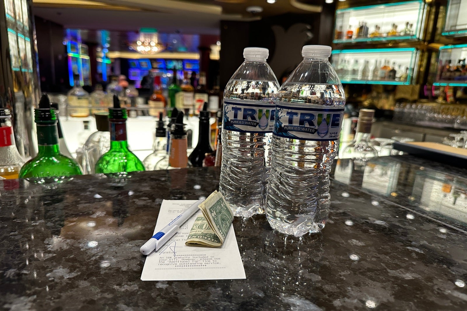 Two bottles of water sitting on top of a bar counter with a recepit, pen and cash next to them