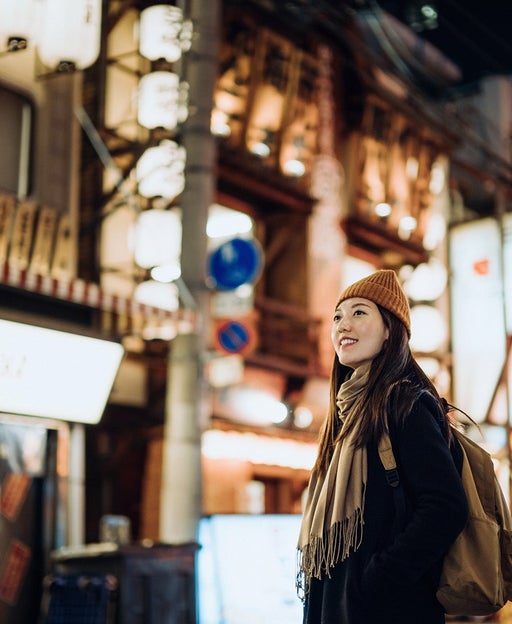 Young Asian female traveller with backpack visiting Japan, exploring and strolling in downtown city street at night in Osaka. A popular nightlife and entertainment area in the city. Travel, vacation and holiday concept