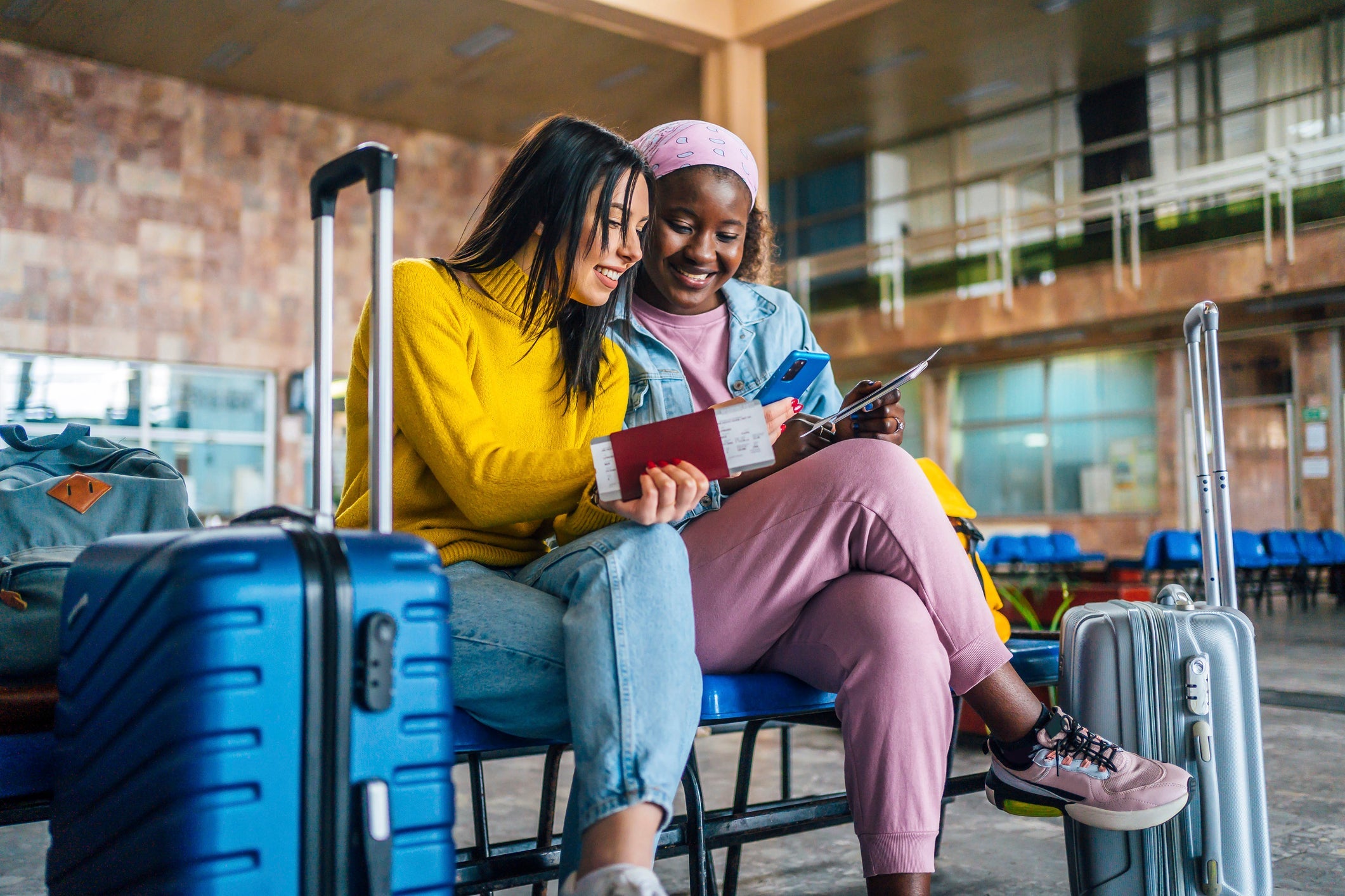 Young cheerful multi racial women friends looking at mobile phone at the airport while waiting for their flight.