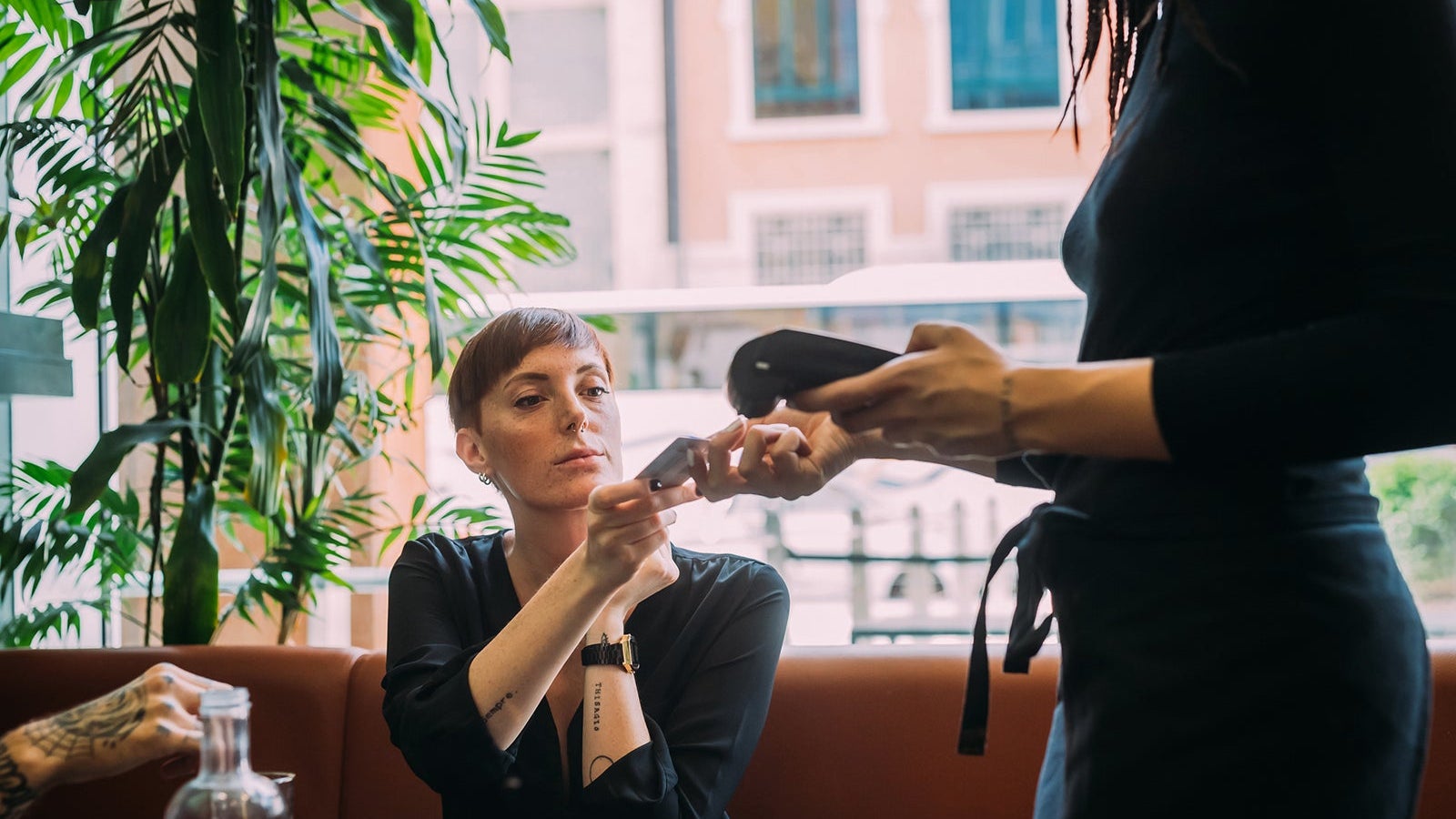 Young woman with short hair sitting in a bar, using credit card to pay.
