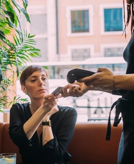 Young woman with short hair sitting in a bar, using credit card to pay.