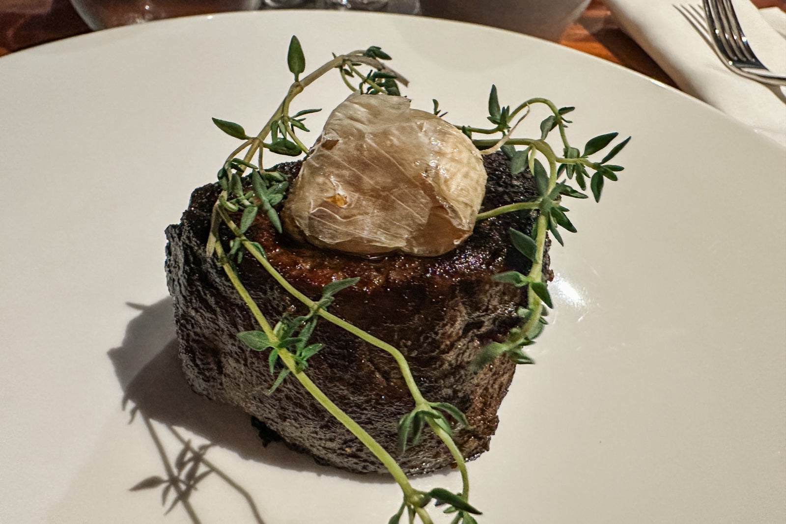Steak on a white plate topped with herbs and garlic