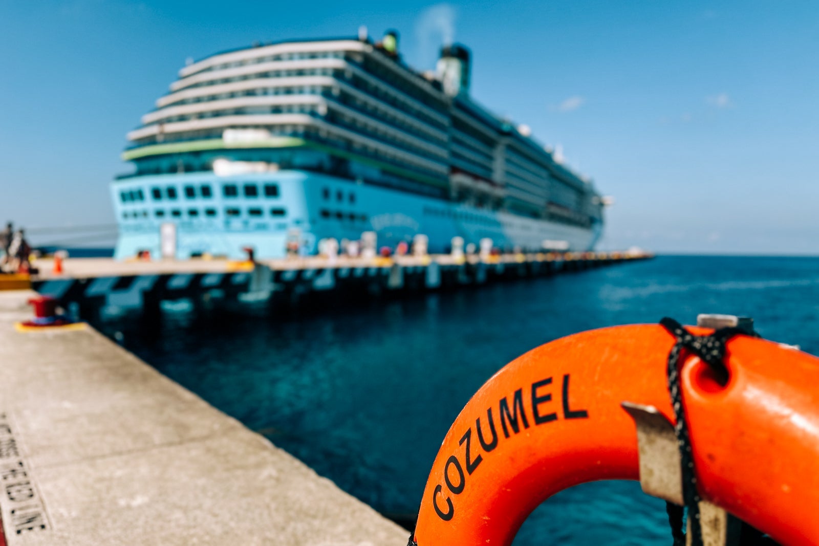 An orange life ring that says "Cozumel" mounted on a the dock with Margaritaville at Sea's Islander cruise ship docked in the background