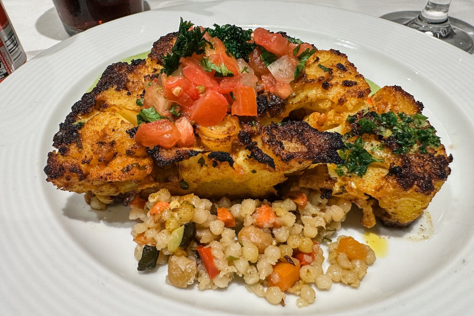 A cauliflower steak on a plate with vegetables and couscous