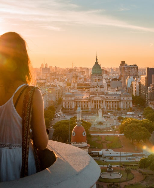 Rear View Of Woman Standing At Balcony Against Cityscape During Sunset