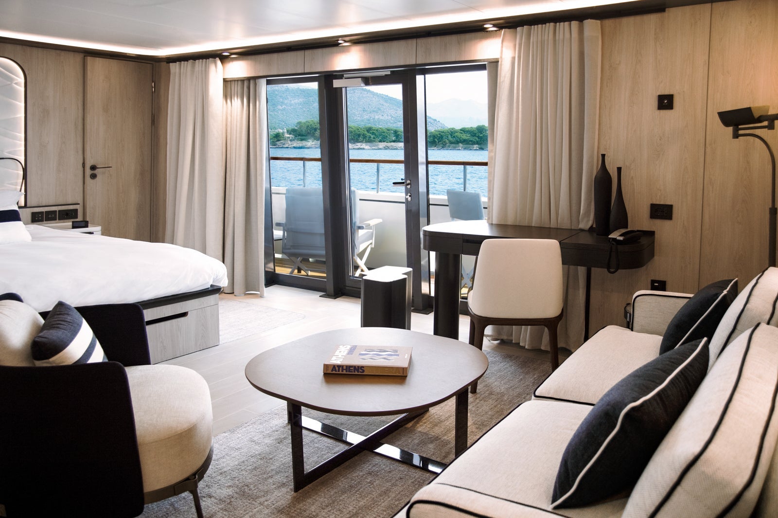 A spacious suite with a bed, living room and a large balcony with water and mountains in the distance