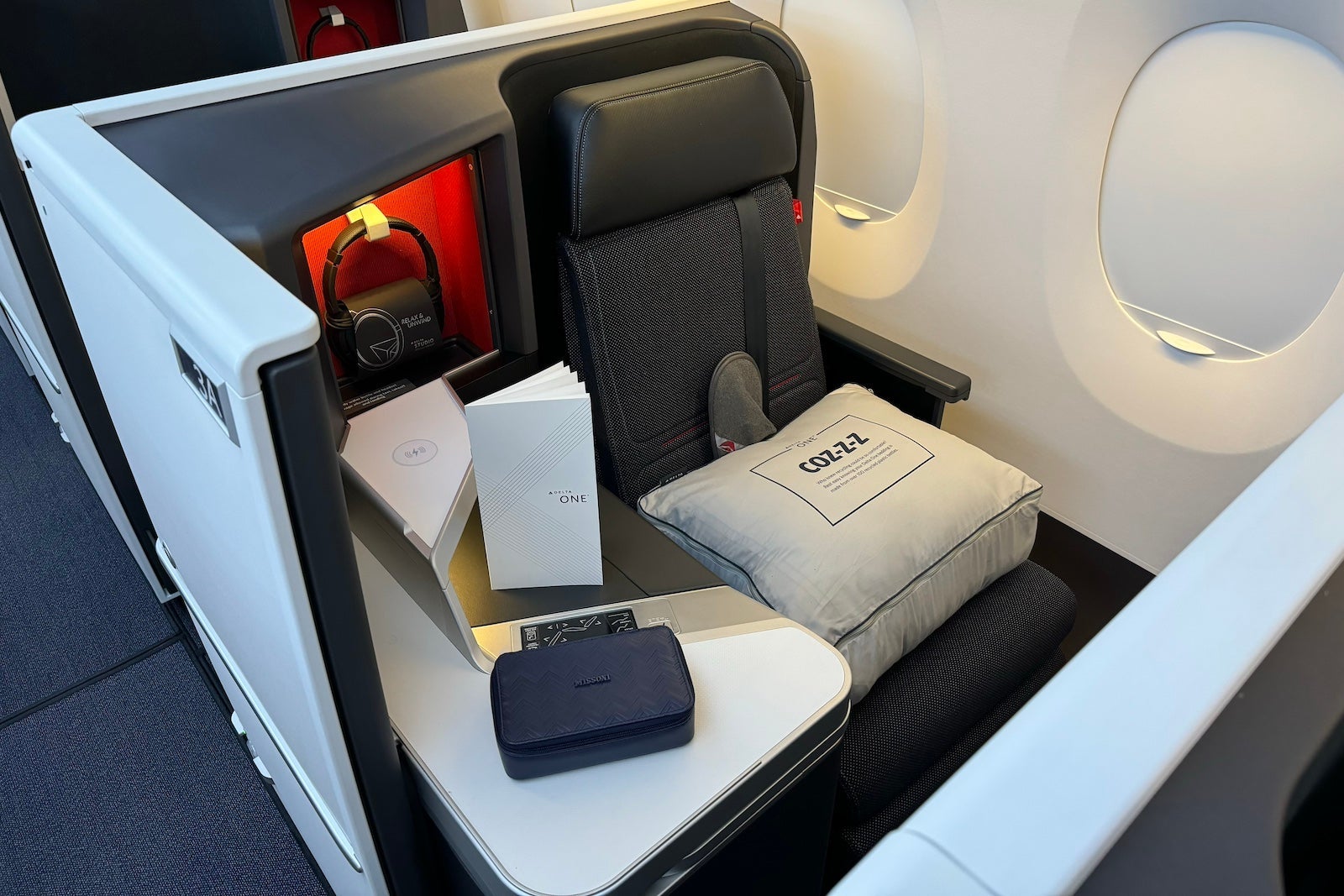 an airplane seat with privacy wall, amenity kit, headphones and blanket