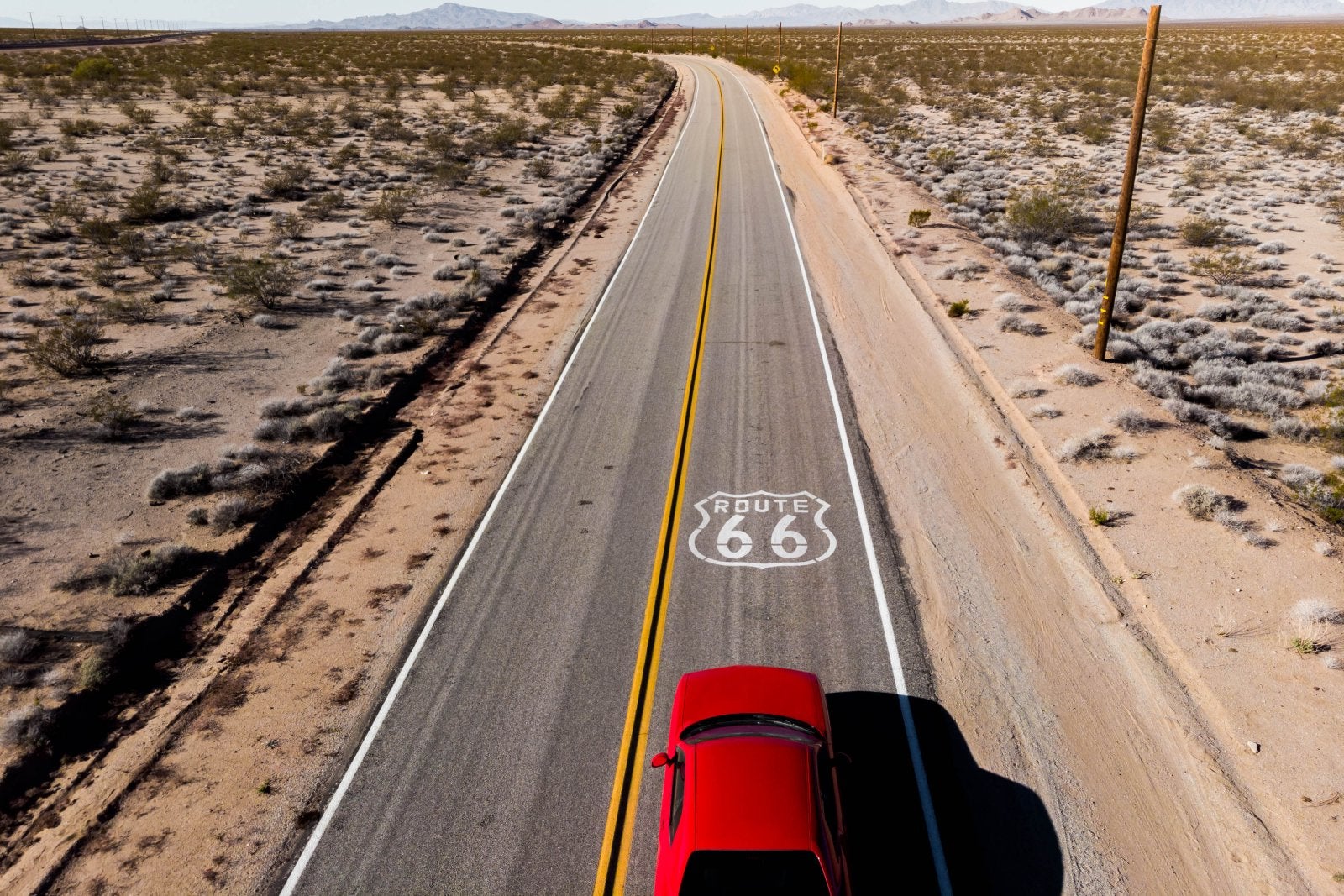 Drone view of American car driving in a straight road at the California desert.