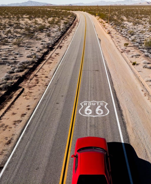 Drone view of American car driving in a straight road at the California desert.