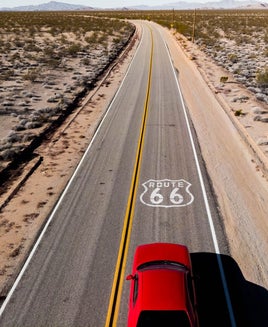 Drone view of American car driving in a straight road at the California desert.