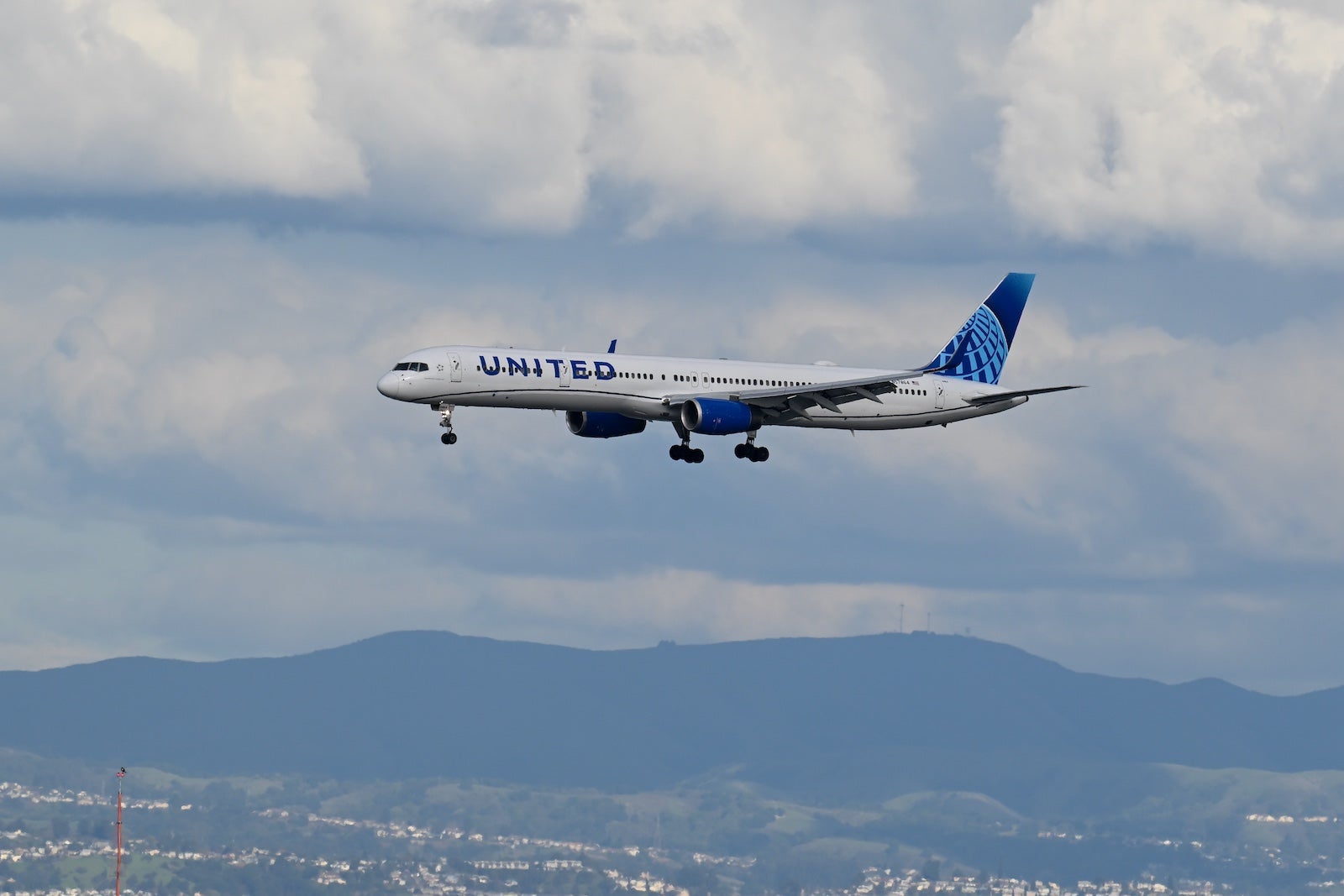 A United Airlines plane with a cloudy sky and hills in the background