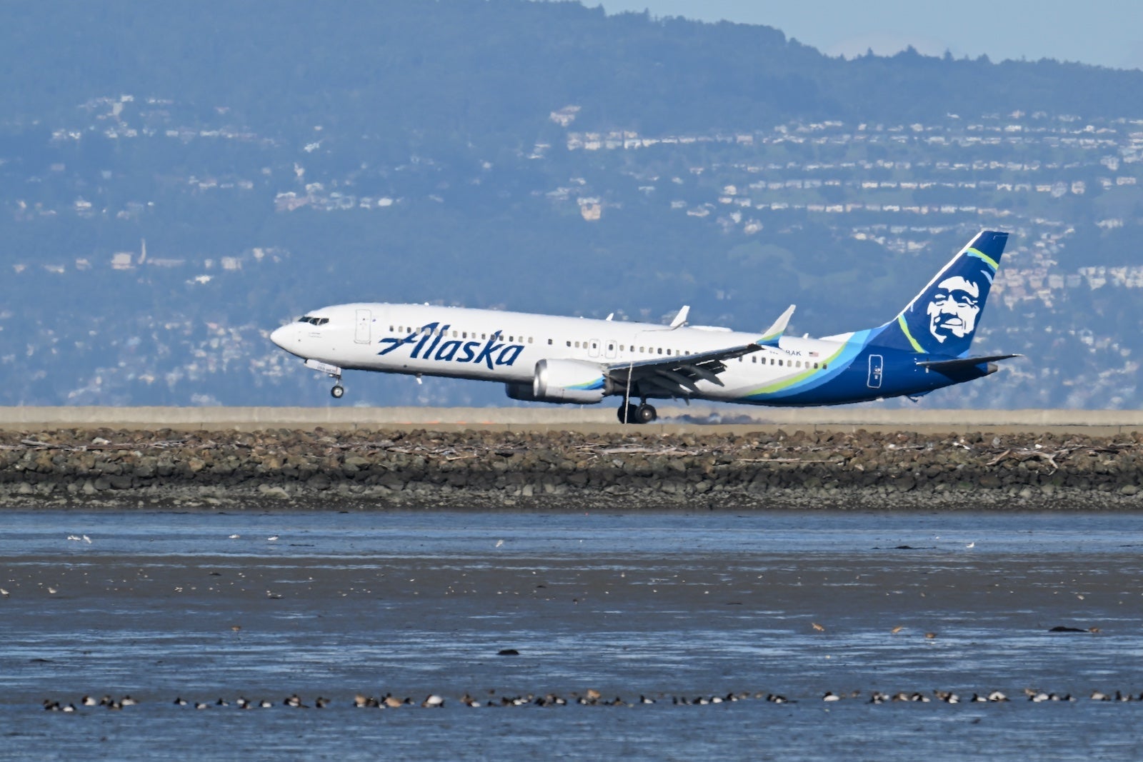 An Alaska Airlines plane flies low over water near San Francisco International Airport