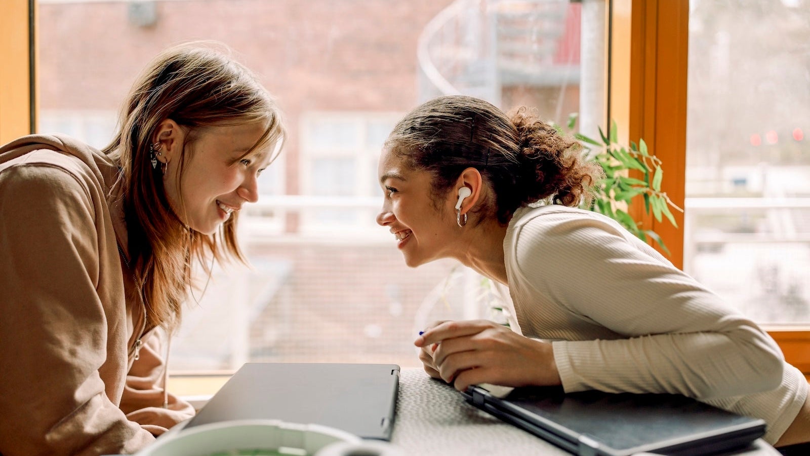 Smiling female teenage friends gossiping with each other at high school