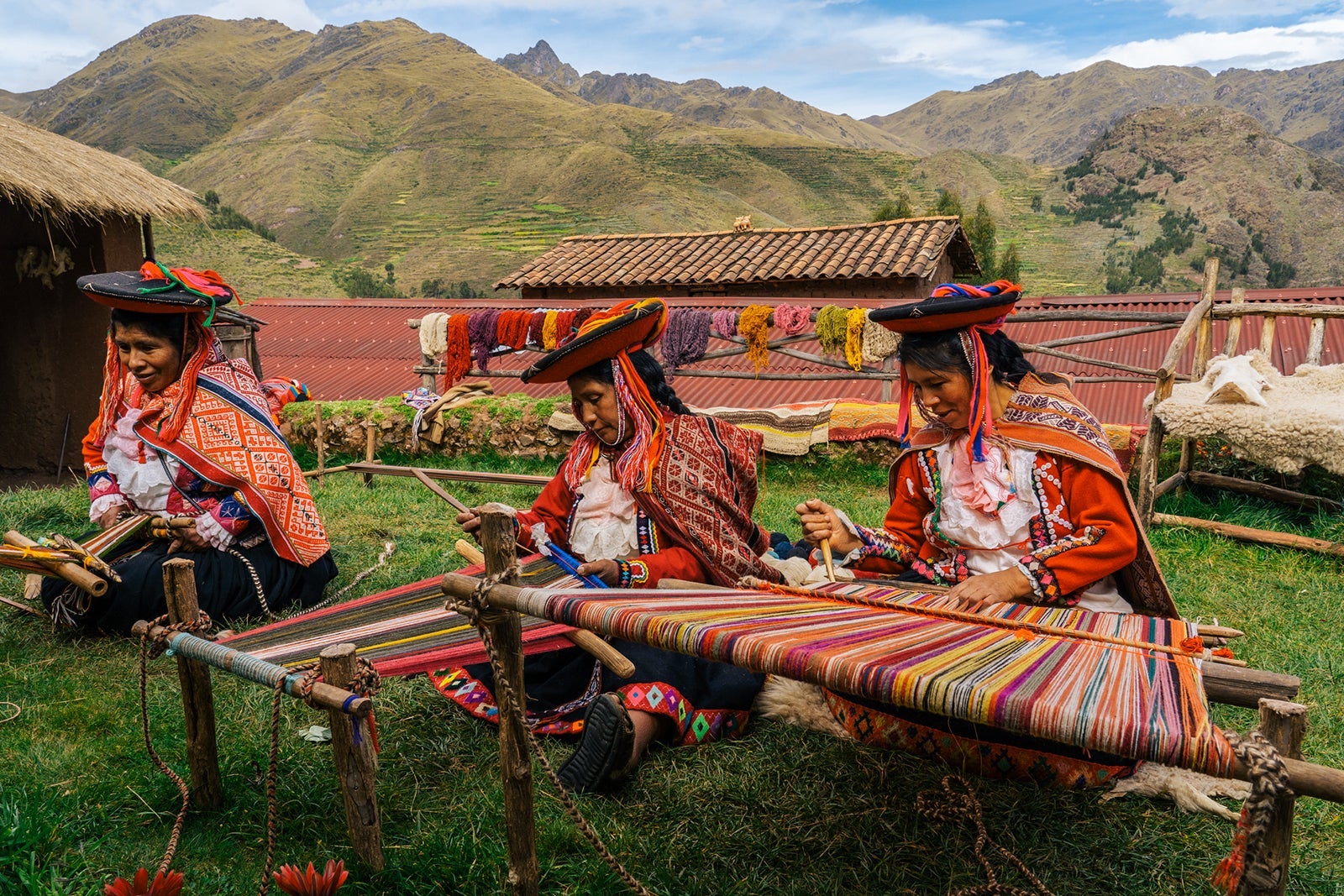 Three local female weavers in colourful traditional local dress including festooned hats, weaving colourful alpaca wool on the ground, Chumbe Community, Lamay, Sacred Valley, Peru (3 Model Releases)