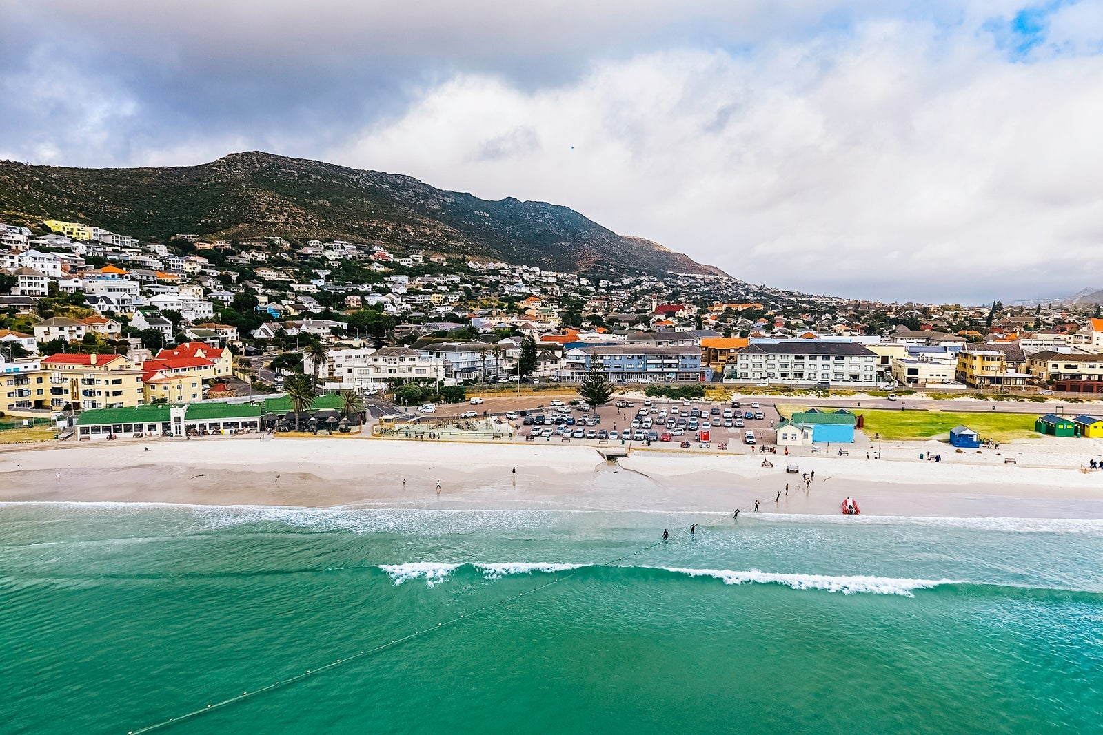 Muizenberg Beach is a surfers favourite beach situated in False Bay, Cape Town, seen here the main beach with surfers at sea and beach parking lot.