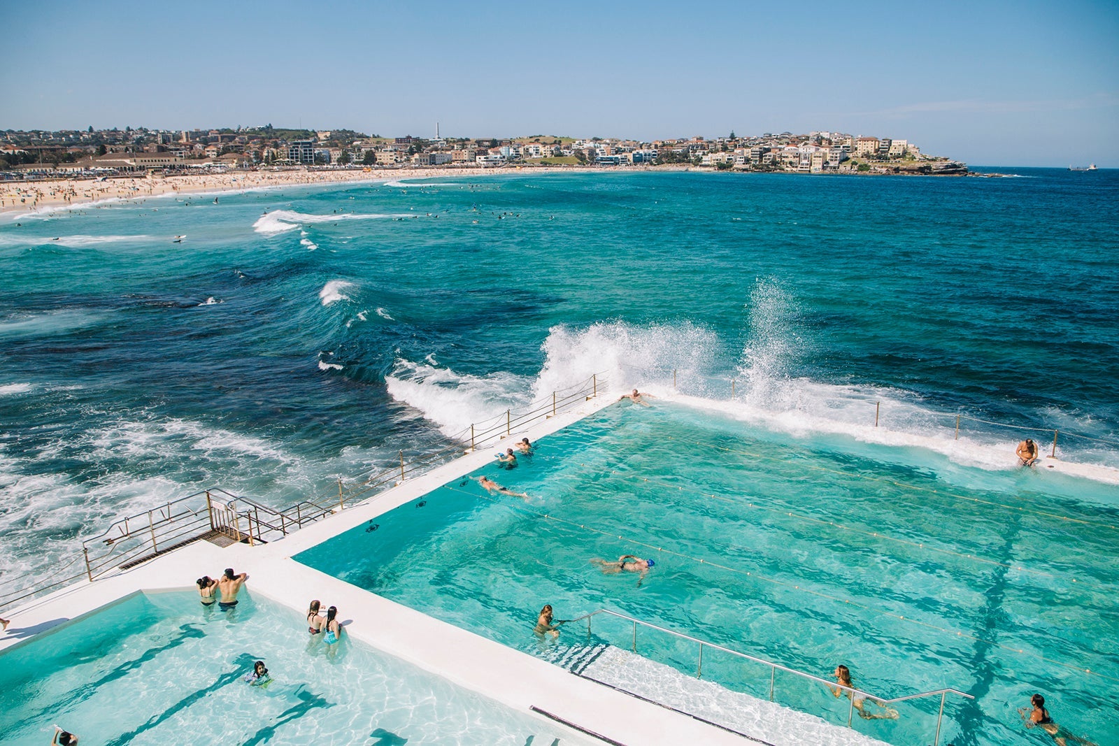 People swimming in the fresh water swimming pools built in to the sea with waves rolling in to Bondi and breaking against the edge of the pool