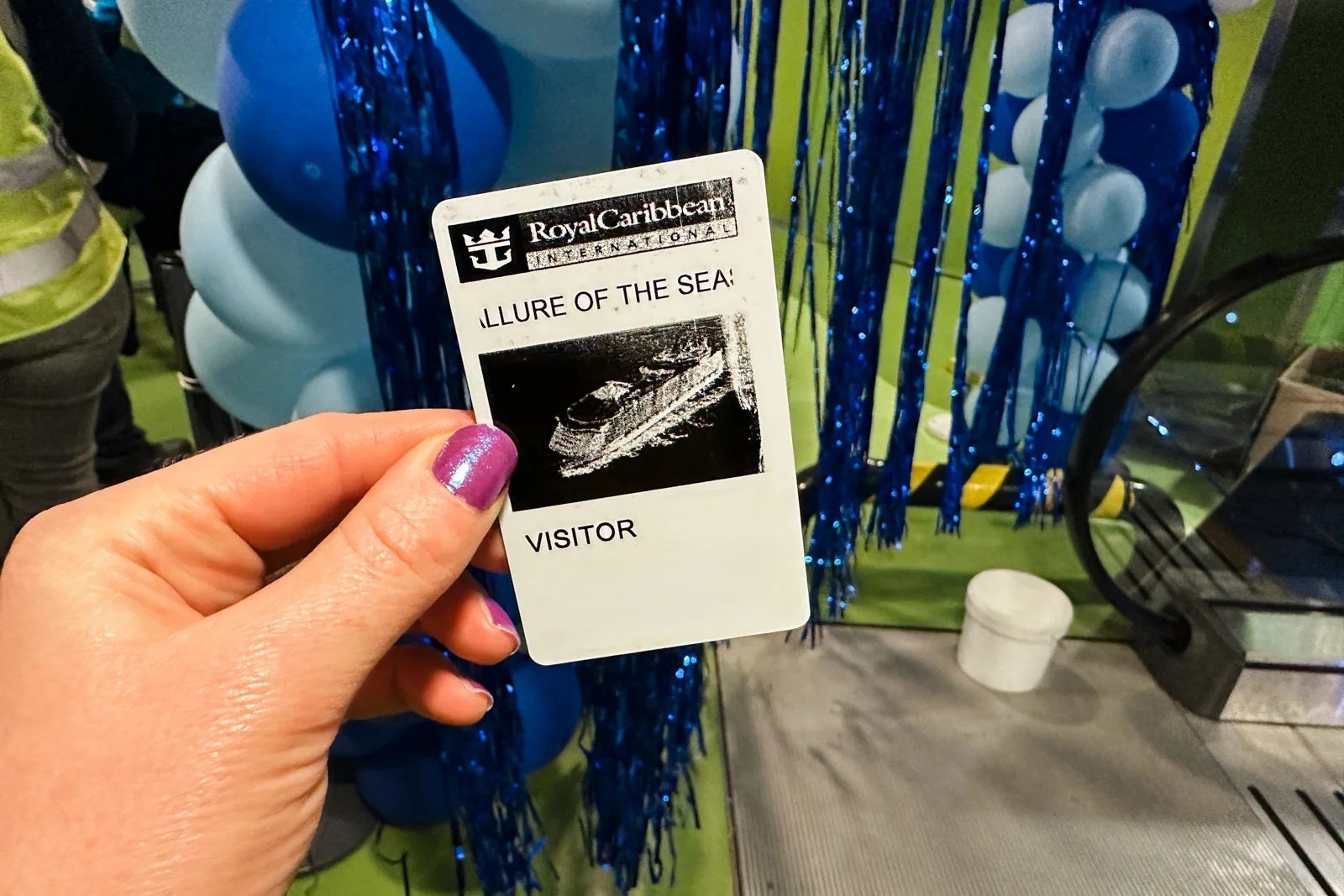 A hand with purple nail polish holding a visitor pass for cruise ship Allure of the Seas