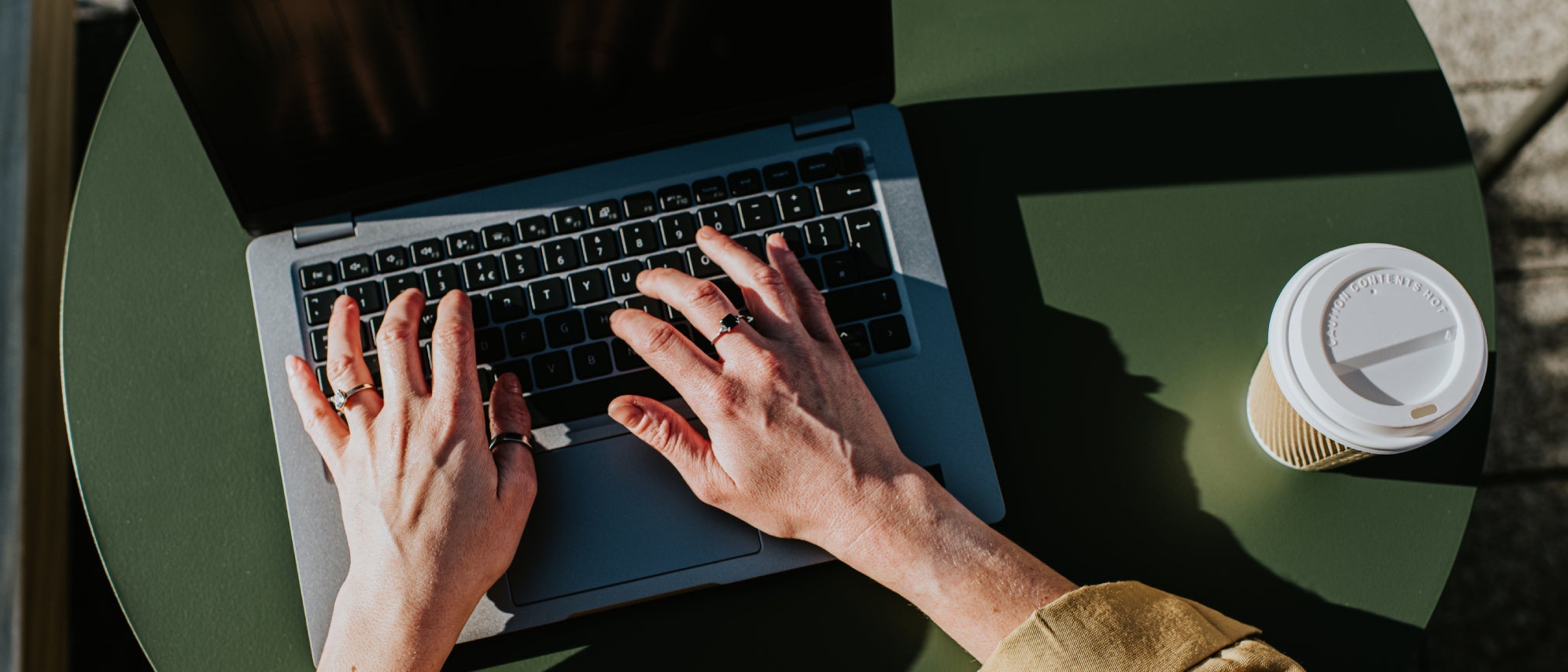 Hands typing on a laptop keyboard with a cup of coffee