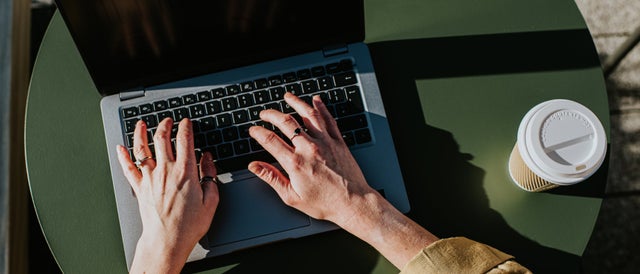 Hands typing on a laptop keyboard with a cup of coffee
