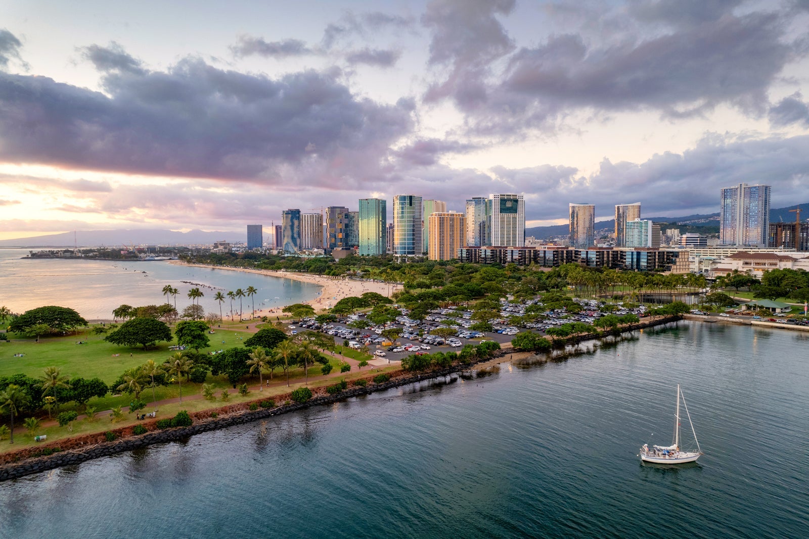 Aerial view of Oahu with sandy beach and green park in the foreground and skyscrapers in the distance