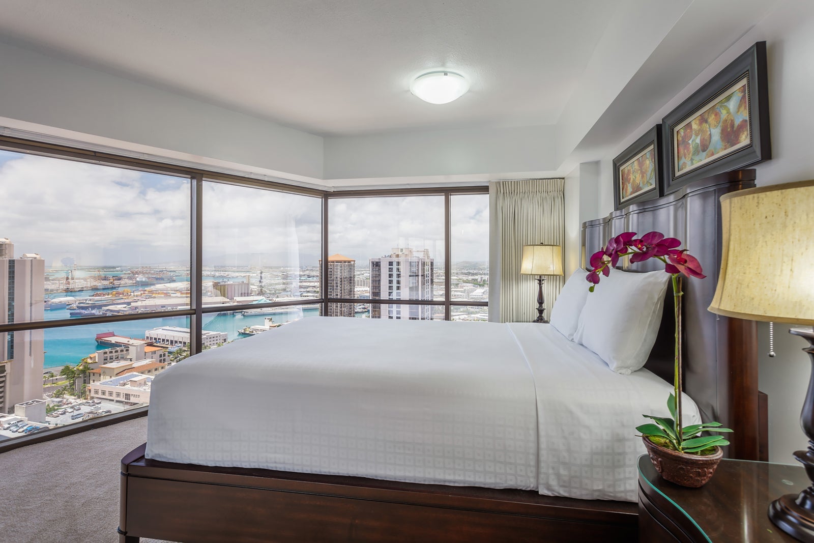 Hawaii hotel room with bed with white linens and walls of windows overlooking the water
