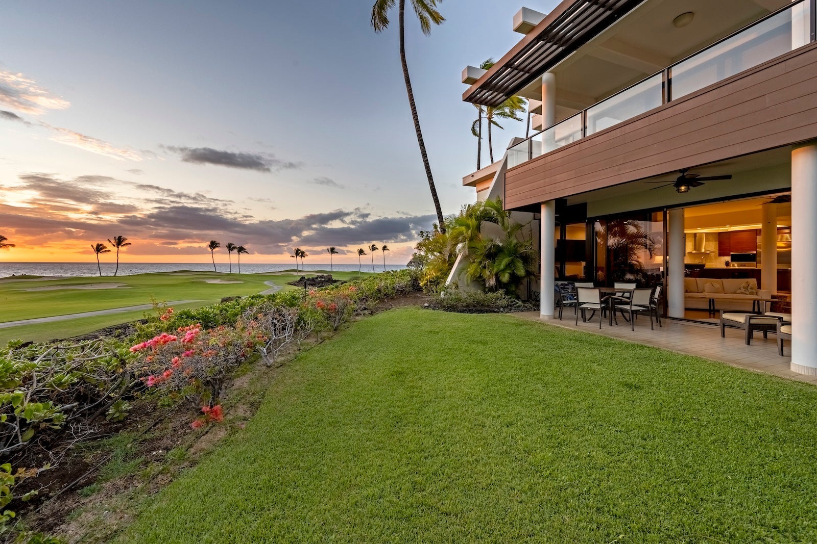 two-story condo building with grassy lawn, ocean, sunset and tall, skinny palm tree