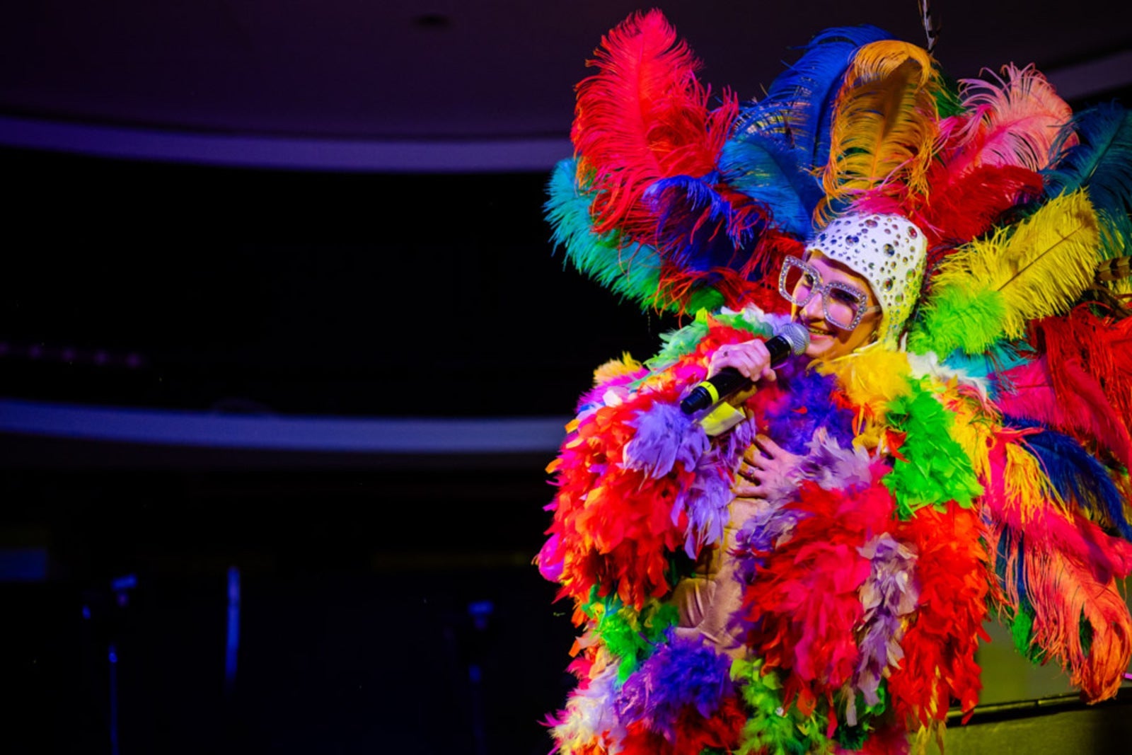 An Elton John tribute performer on stage covered in colorful feathers and big glasses