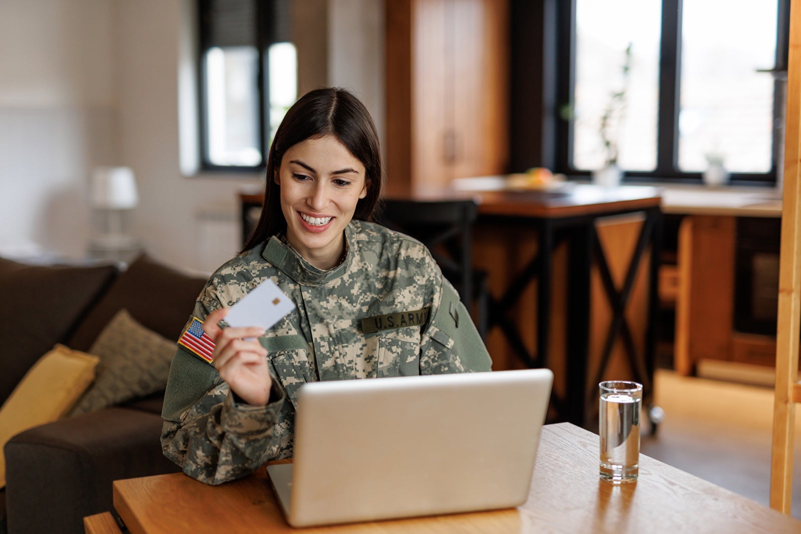Smiling US Army soldier shopping online using laptop and credit card at home