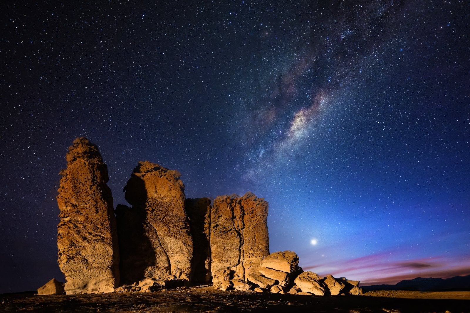 This picture shows a rock formation at the Salar de Tara in front of the Milky way at night. Also on the night sky is the planet venus visible at the horizon.