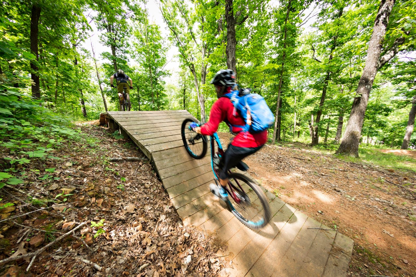 mountain biker rides over a wooden ramp on a downhill trail at Slaughter Pen mountain bike park in Bentonville, Arkansas