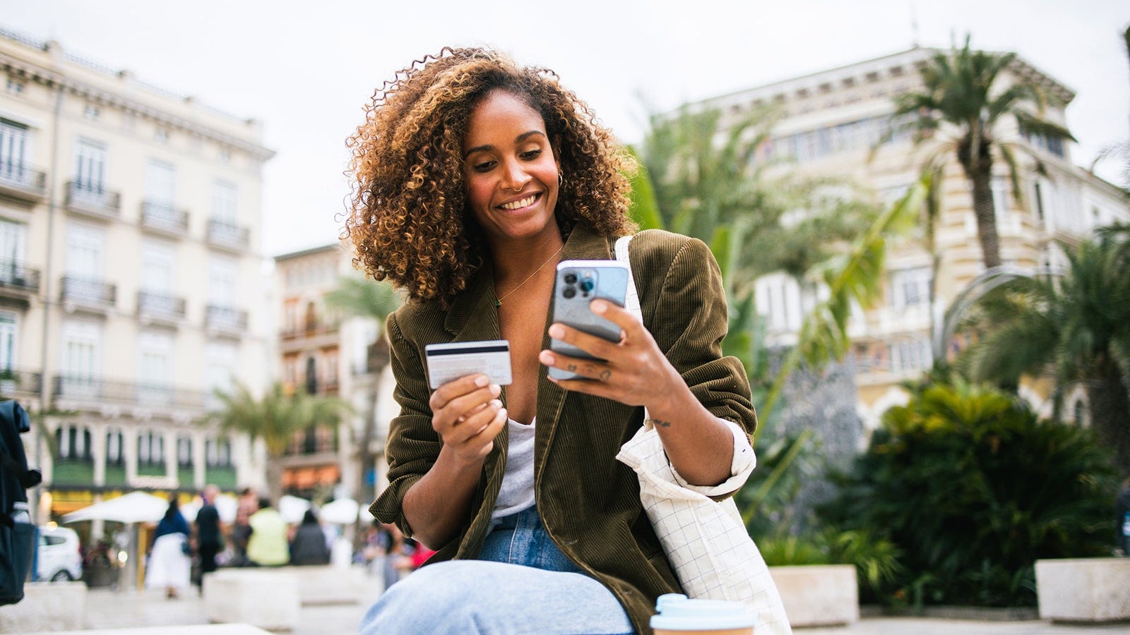 Happy woman enjoying coffee on the street and shopping online