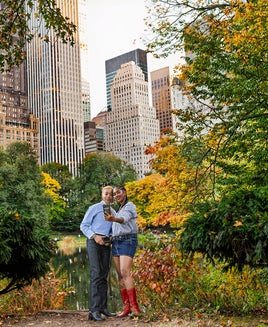 couple taking selfie in Central Park in autumn showing leaves turning shades of yellow and orange with skyscrapers in the background
