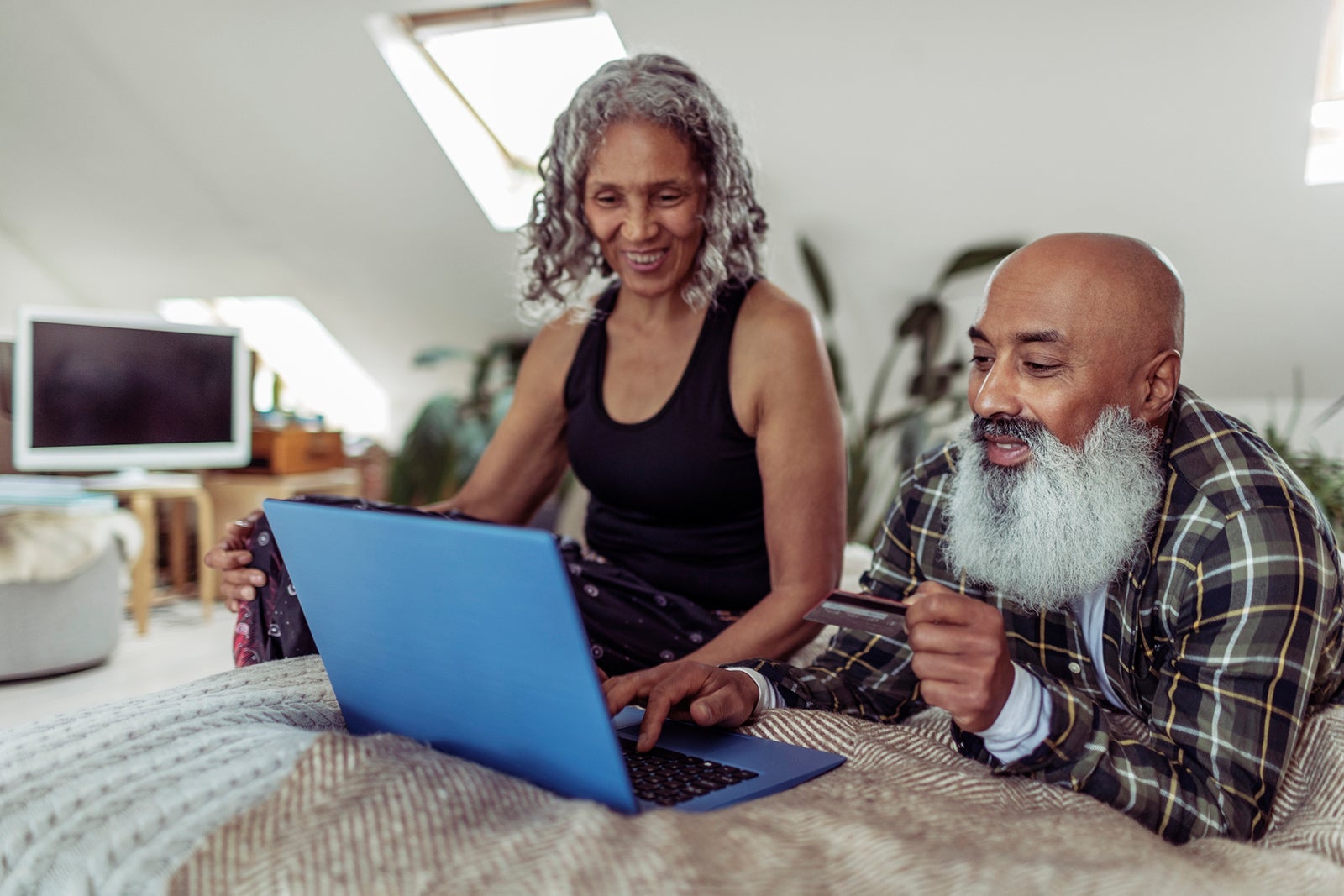 Couple with credit card using laptop while in bed Caia Image