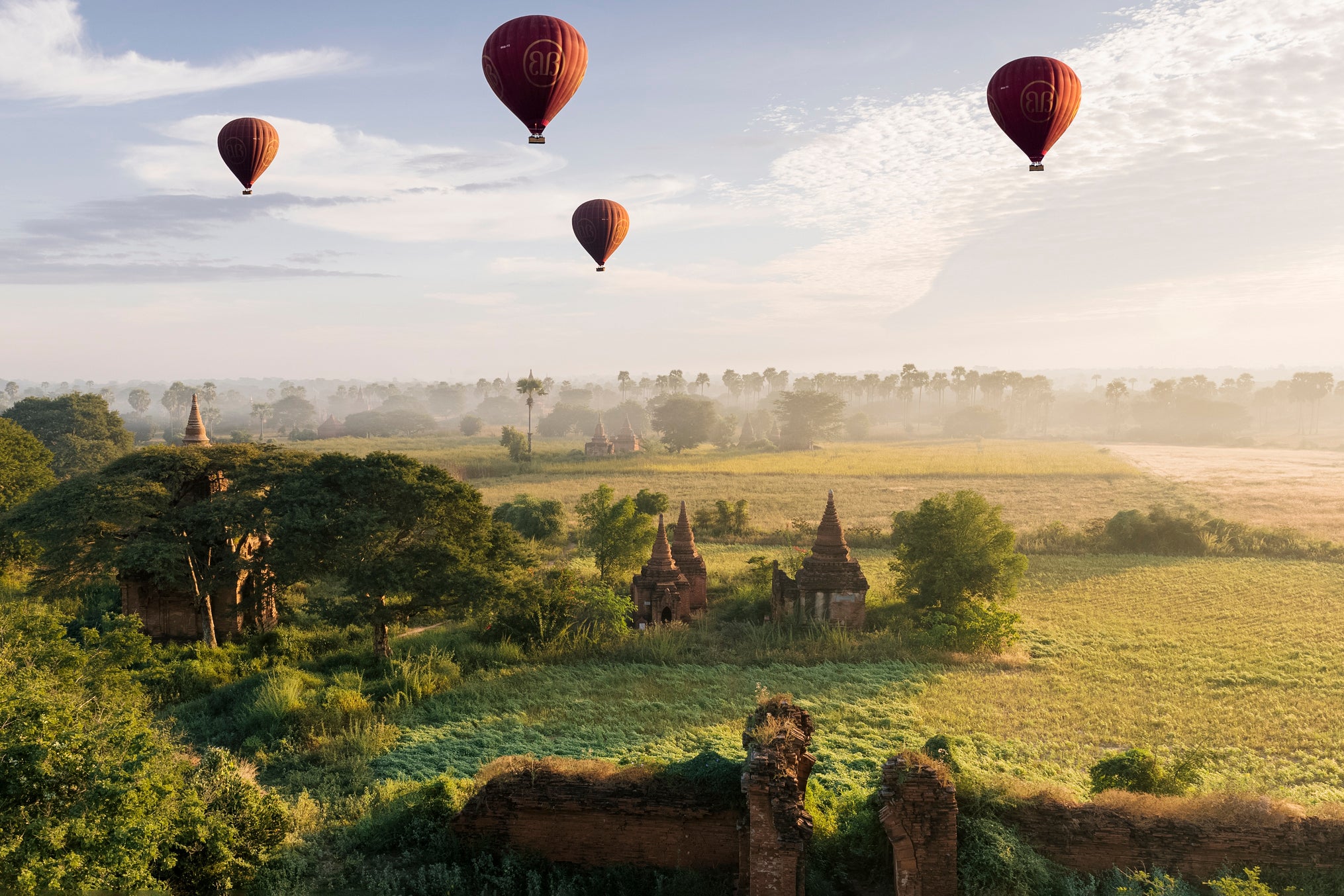 Asia, Myanmar, Bagan, hot air balloons flying over ancient temple ruins at sunrise, carrying tourists on balloon rides
