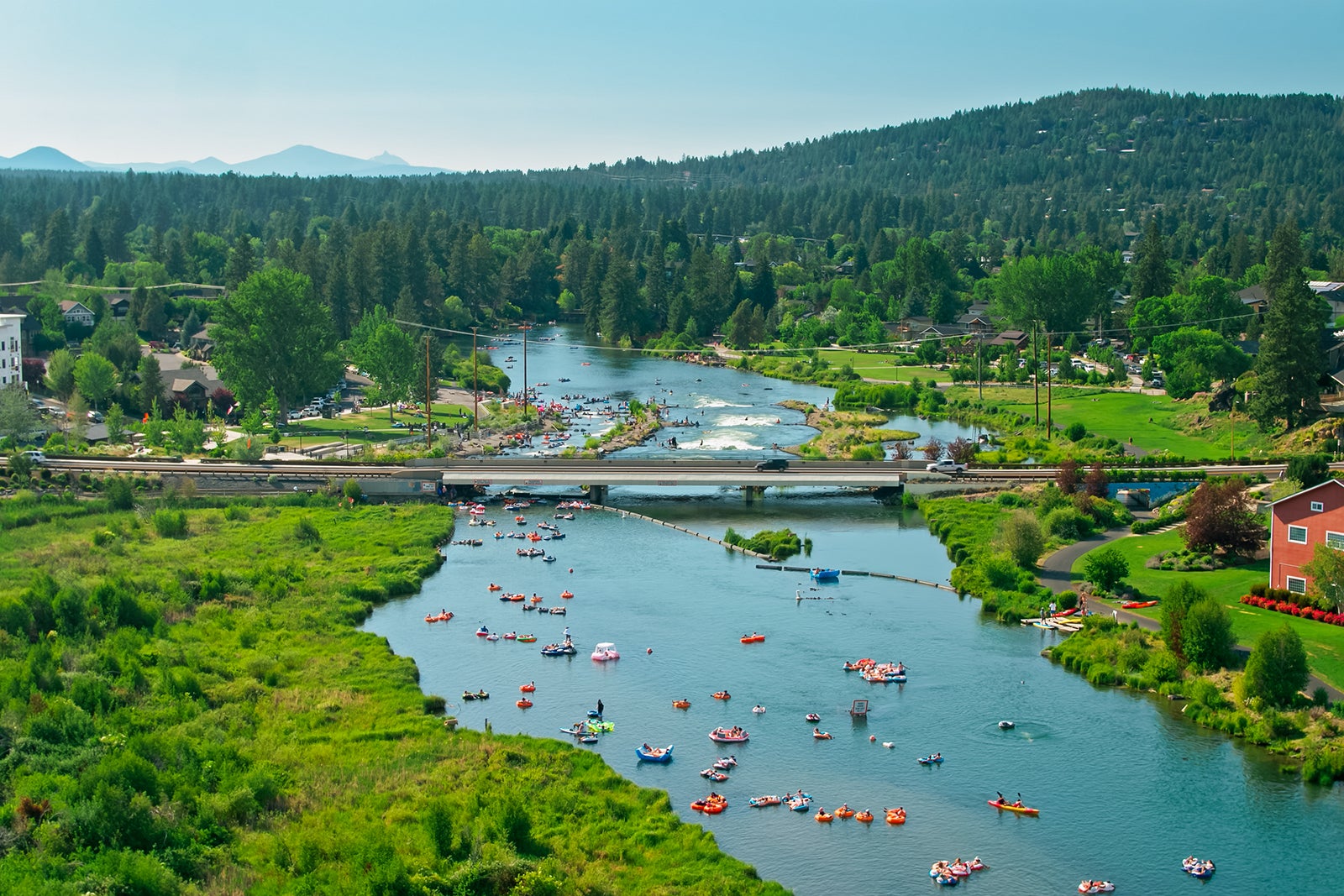Aerial establishing shot of Bend, Oregon, on a hot and sunny day in summer. Scores of people are tubing, paddleboarding, kayaking and surfung in the water of the Deschutes River, especially around the Whitewater Park, a set of artificial rapids and waves.
