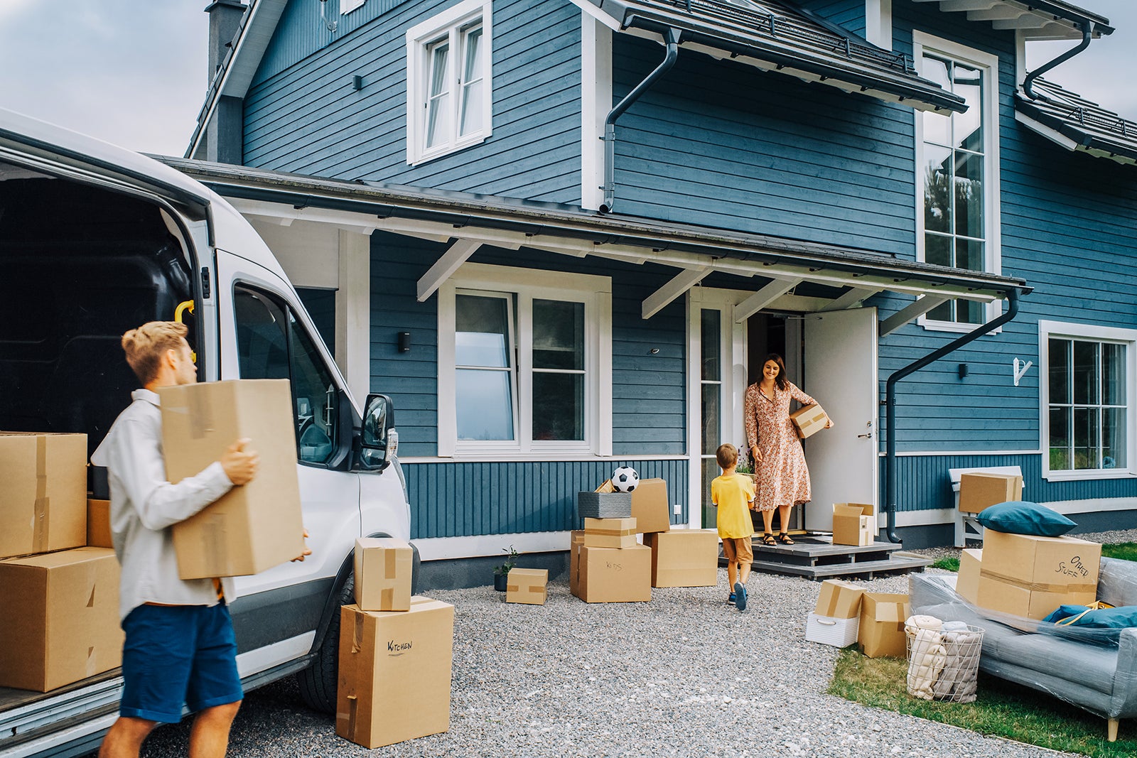Young Son Helping Parents to Unload a Cargo Van with Furniture and Accessories for Their New Home in SUccessful Residential Area. Kid Bringing a Plant to His Mother. Family Moving to Their New Home.