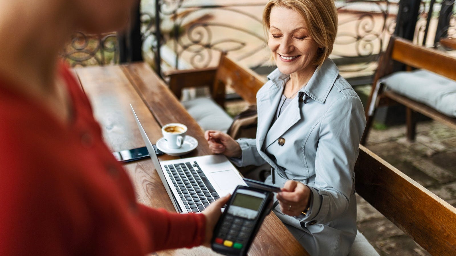 Mid adult businesswoman working with a laptop in a coffee shop paying with credit card