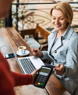Mid adult businesswoman working with a laptop in a coffee shop paying with credit card