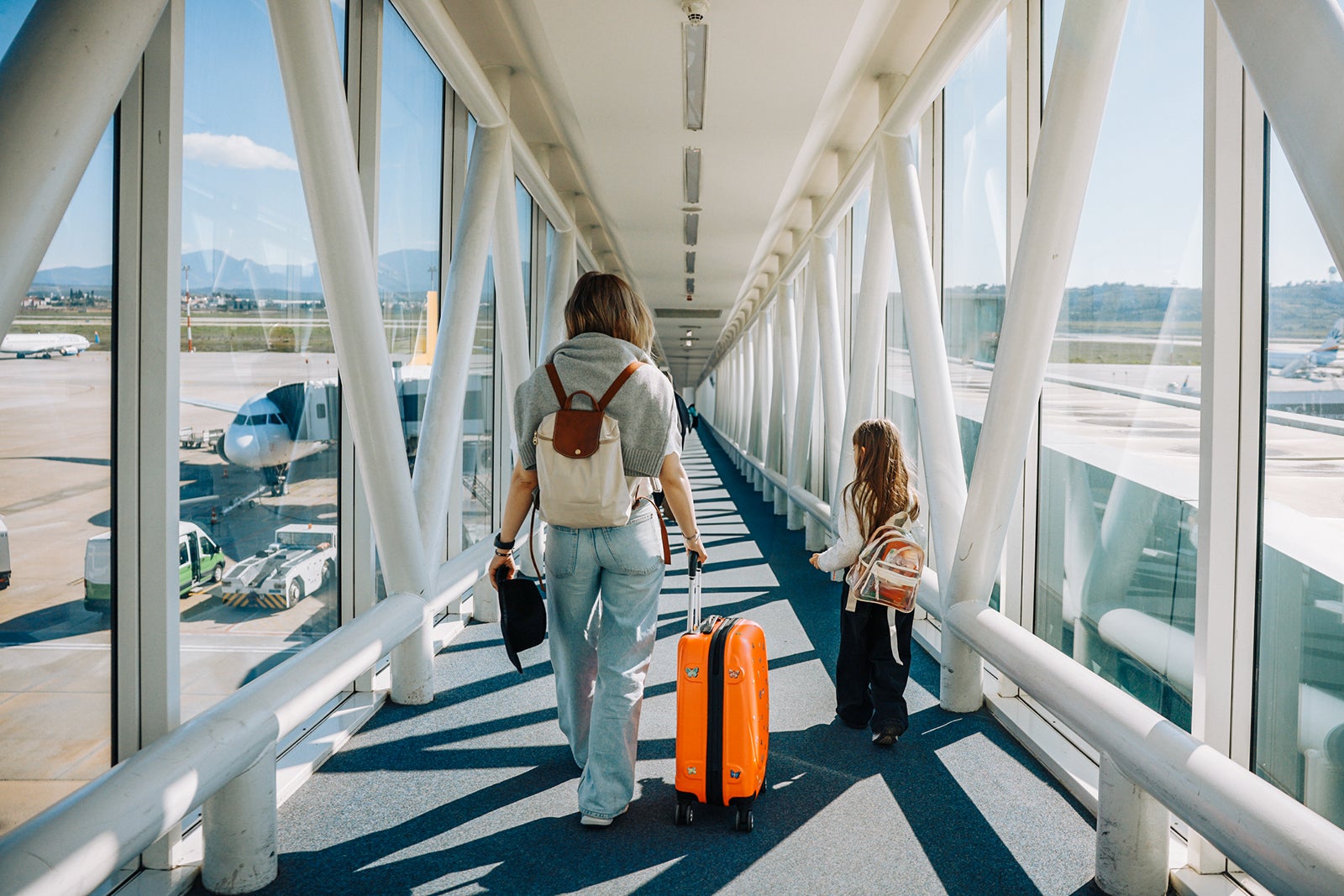 Airport: A beautiful mother and a beautiful little daughter expecting their vacation plane, looking outside the arrival window and travel. A little family in Loading Lounge of Airline Hub