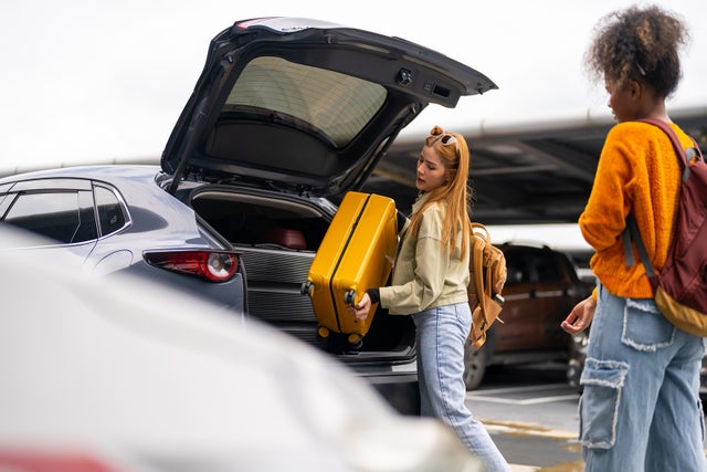 Woman passenger with passport travel by air transportation. Woman friends taking off luggage from car trunk in Airport parking and walking to airline check in counter at airport terminal.