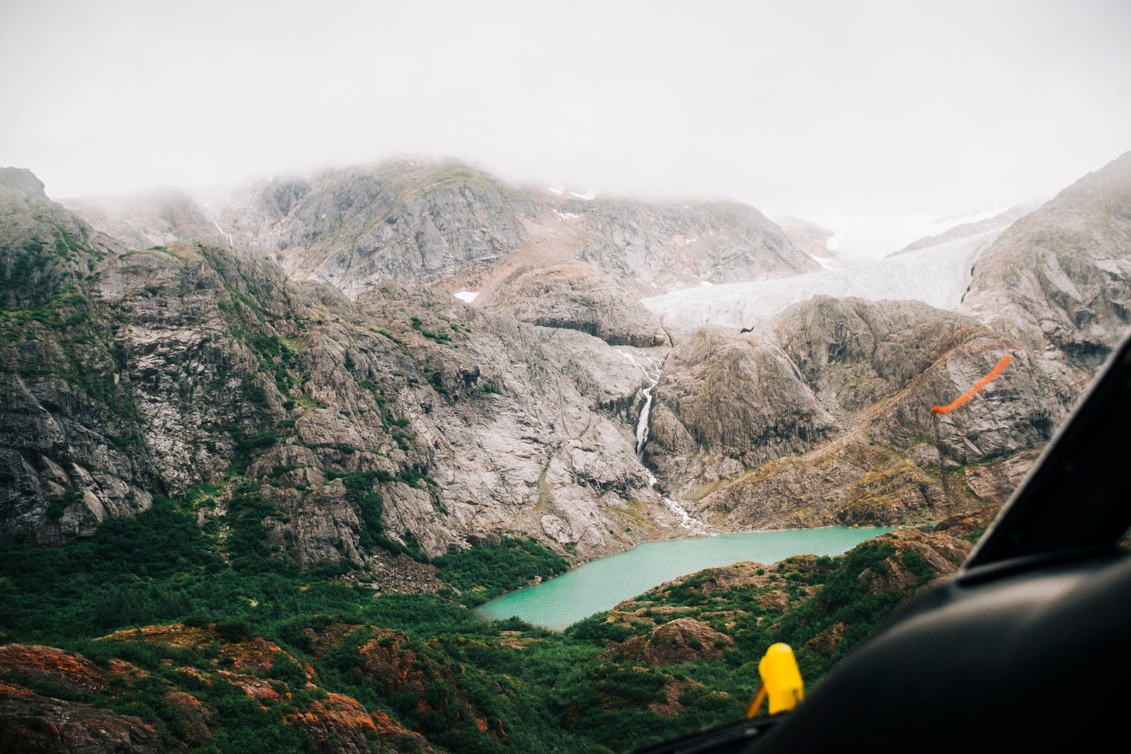 Aerial view of gree glacial lake and a waterfall descending from the Lemon Glacier in Juneau Icefield seen through a helicopter window in transit, Juneau, Alaska, USA