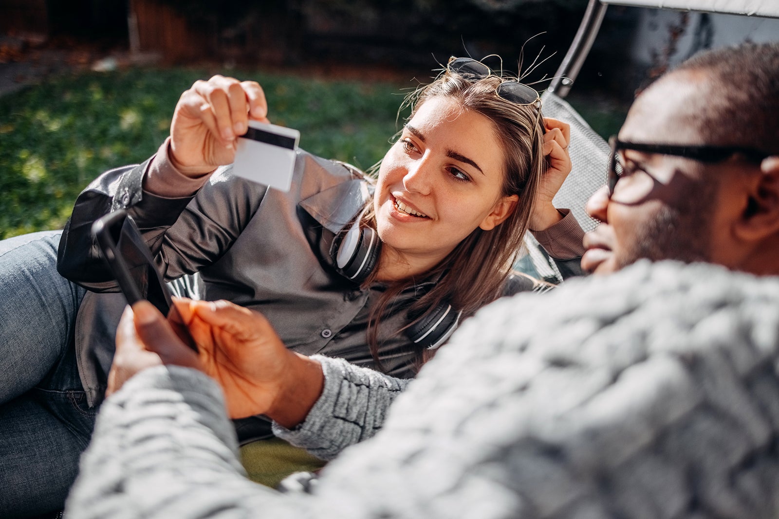 Multiethnic young couple using smartphones on autumn sunny day shopping at home in their backyard
