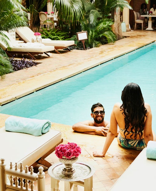 Wide high angle shot of couple relaxing at edge of pool in courtyard of luxury hotel while on vacation