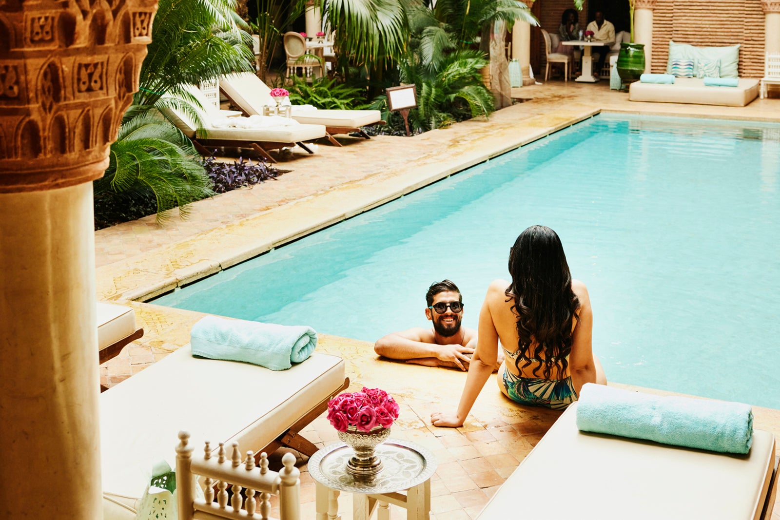 Wide high angle shot of couple relaxing at edge of pool in courtyard of luxury hotel while on vacation