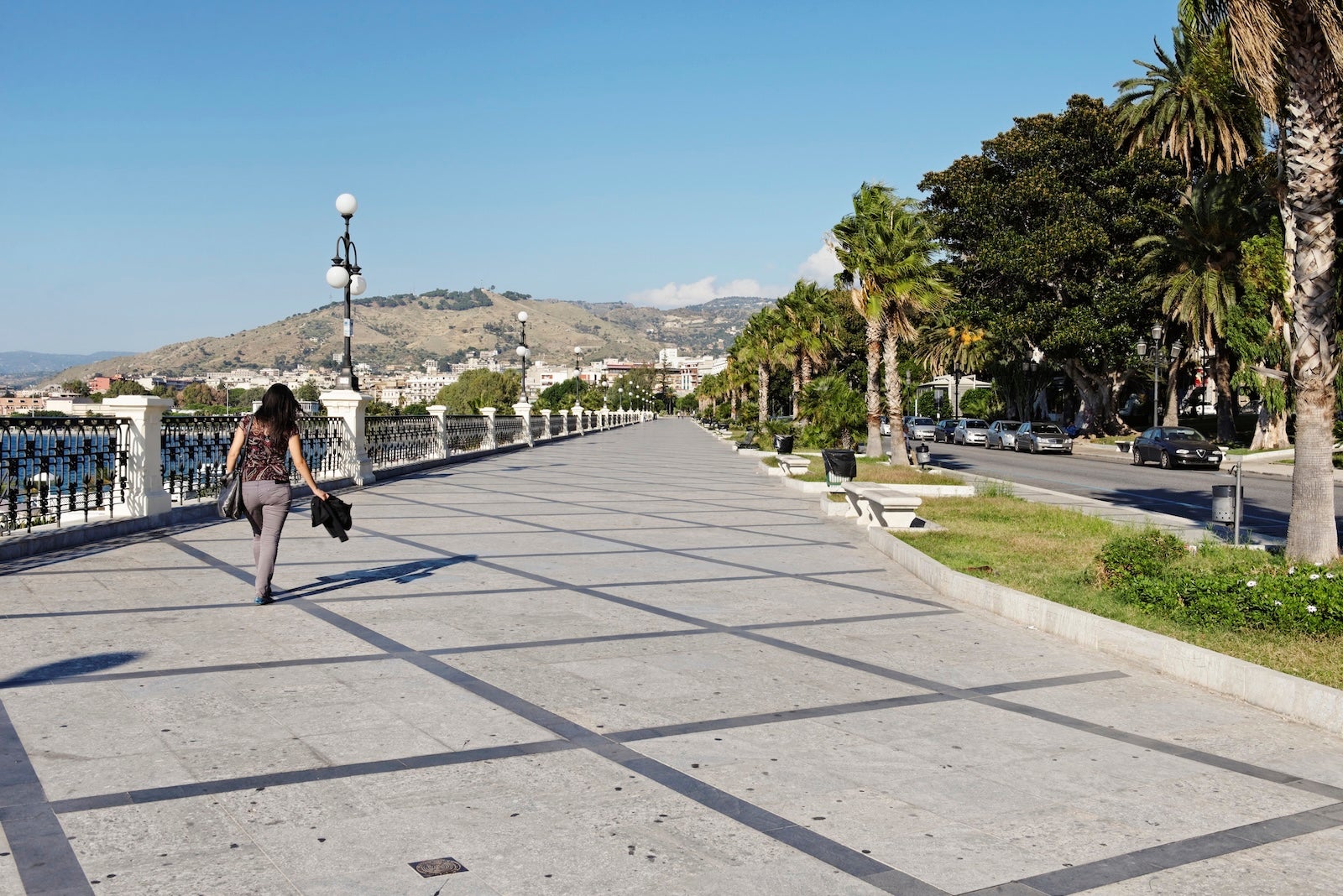 Here's why you should go to Calabria instead of Rome or Milan Reggio di Calabria,Calabria,Italy - September 27, 2013: Waterfront promenade ( lungomare ) of Reggio di Calabria, the capital of the province of Reggio Calalabria in Southern Italy. This city is also located at the Strait of Messina which separates it from Sicily. A woman is passing by.